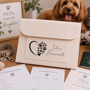 May include: A cream-colored felt document folder featuring a black graphic of a heart made of paw prints and the text "Lola's Documents". The folder is accompanied by three white paper forms labeled Pet Health Record, Vaccination Record, and Pet Insurance.