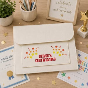 May include: A cream-colored felt document folder with a flap closure, featuring the red text "OLIVER'S CERTIFICATES" and a pattern of small orange and yellow stars printed on the front pocket, designed for organizing and storing various paper certificates.