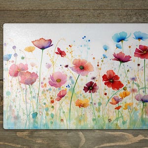 May include: A watercolour painting of a field of colourful wildflowers. The flowers are painted in shades of pink, red, blue, and yellow. The background is a soft white with a light blue wash.