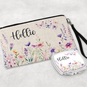 Peut inclure: Une trousse de maquillage en toile beige et un petit miroir compact, tous deux ornés d'un motif floral dans les tons de rose, violet et jaune. Le nom "Hollie" est écrit en cursive sur les deux articles. Le sac a une fermeture éclair noire et une dragonne.