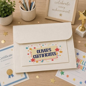 May include: A cream-colored document folder with a flap closure, featuring a rectangular label printed with the text "OLIVER'S CERTIFICATES" surrounded by colorful star and confetti graphics in shades of red, yellow, blue, and green.