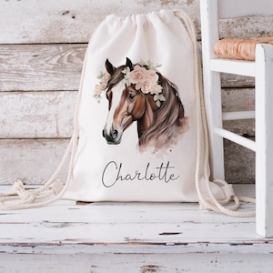 May include: A white drawstring bag with a brown horse illustration wearing a floral crown. The bag has the name "Charlotte" printed on the front.