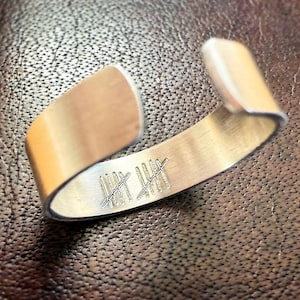 May include: A silver metal bracelet with a series of etched lines on the inside.