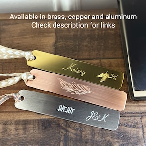 May include: Three metal bookmarks in brass, copper, and aluminum. Each bookmark has a decorative design and a ribbon. The brass bookmark has the name "Krissy" and a bird design. The copper bookmark has a feather design. The aluminum bookmark has tally marks and the initials "J&K".