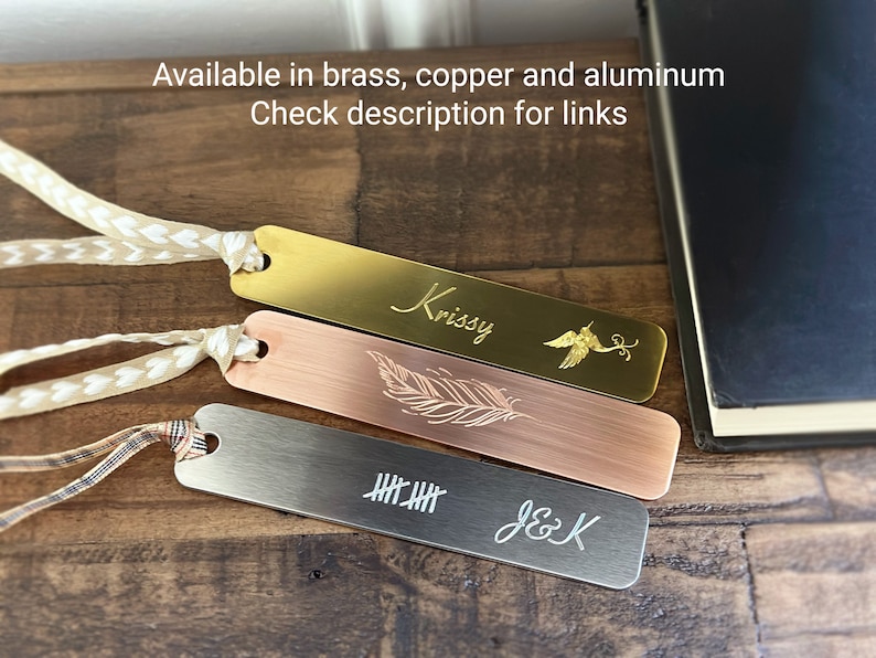 May include: Three metal bookmarks in brass, copper, and aluminum. Each bookmark has a decorative design and a ribbon. The brass bookmark has the name "Krissy" and a bird design. The copper bookmark has a feather design. The aluminum bookmark has tally marks and the initials "J&K".