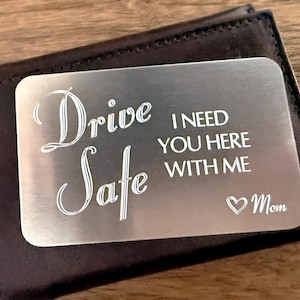 May include: A silver metal card with the text "Drive Safe I Need You Here With Me" and a heart with the word "Mom" engraved on it. The card is in a brown leather wallet.