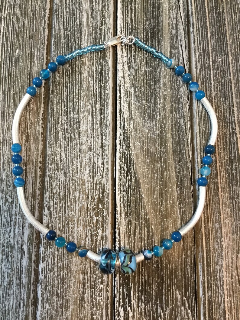 Necklace of blue glass beads and silver colored curved tube beads with sterling silver lobster claw clasp.