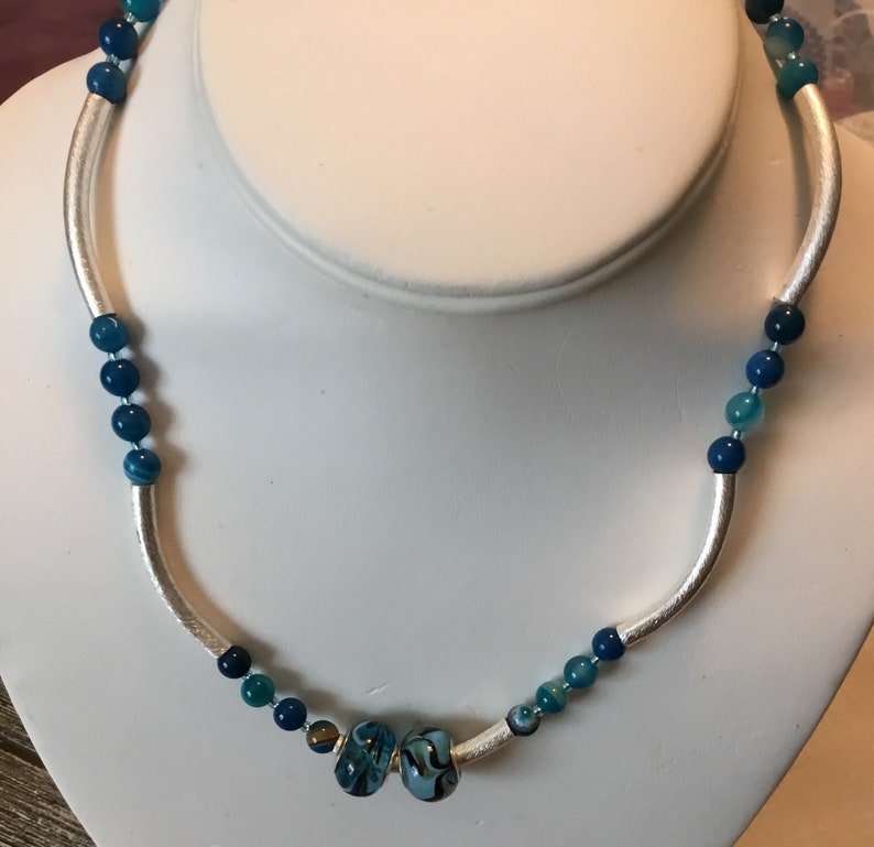 Necklace of blue glass beads and silver colored curved tube beads with sterling silver lobster claw clasp.