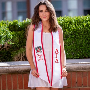 May include: A white graduation sash with red trim and a crest featuring the text "Class of 2025". The sash also features the Greek letters "ΑΓΔ".