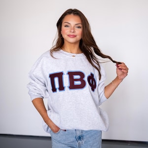 May include: A gray sweatshirt with a maroon and blue embroidered Greek letter design that reads "ΠΒΦ".