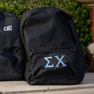 May include: Black backpack with a zippered pocket and the Greek letters "ΣΧ" embroidered in light blue on the front.
