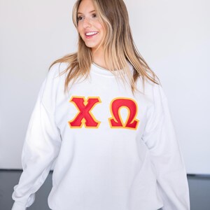 May include: White sweatshirt with red and yellow Greek letters "XO" printed on the front.