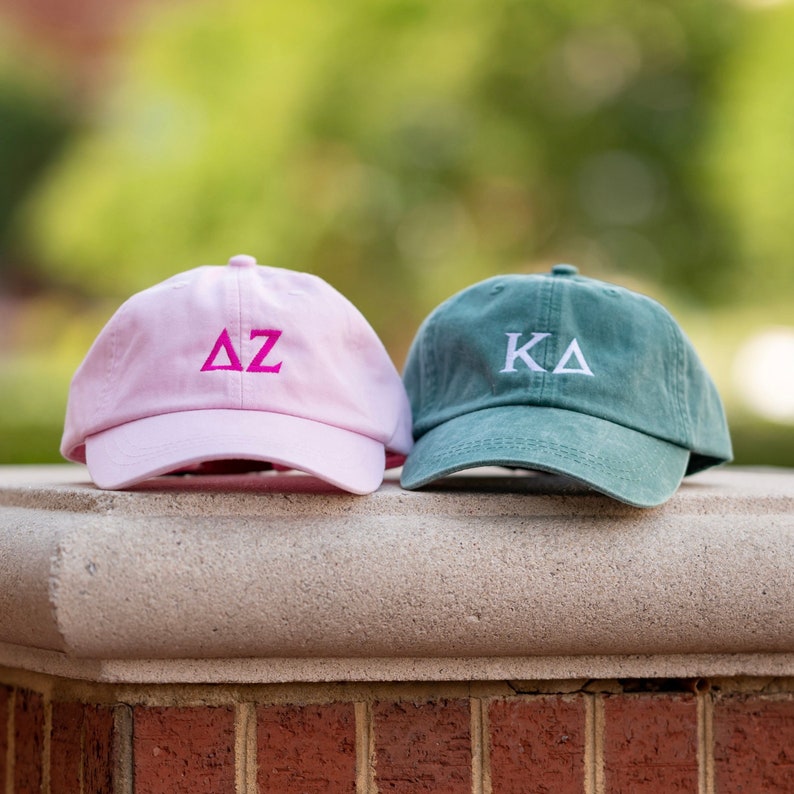 May include: Two baseball caps, one pink with the letters "AZ" in pink and one green with the letters "KA" in white.