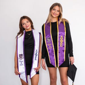 May include: Two people wearing graduation sashes with purple and gold trim. The sashes have the Greek letters Delta Phi Epsilon and the text "Class of 2025".