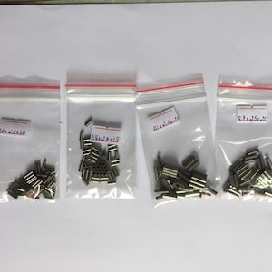 May include: Four clear plastic bags with red zip closures, each containing small, metallic cylindrical objects. Each bag has a white label with black text indicating dimensions: 7.6 x 20 x 14, 5.8 x 24 x 18, 10 x 2.3 x 23, and 9.7 x 15 x 20.
