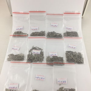 Pode incluir: Conjunto de pequenas pinos de metal prateados em sacos de plástico transparentes. Cada saco contém um tamanho diferente de pino, com as dimensões indicadas em um adesivo branco. Os tamanhos variam de 1,1 x 12,2 a 1,4 x 10,2 polegadas.