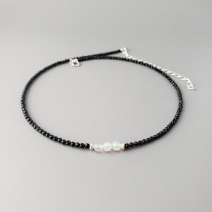 May include: A delicate black choker necklace with three white opal beads in the center.