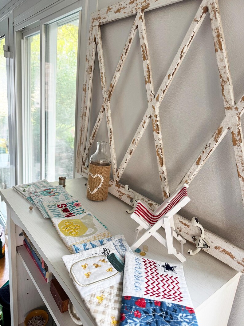 Pu&ograve; includere: Una cornice in legno bianco anticato con un motivo a rombi &egrave; montata su un muro. Una bottiglia di vetro trasparente avvolta in iuta con un design a cuore &egrave; appoggiata su una mensola bianca, insieme a oggetti trapuntati e una sedia a sdraio in miniatura.