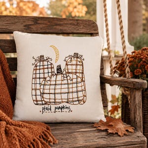 May include: A square off-white throw pillow featuring an embroidered design of three pumpkins with a plaid pattern in black and orange thread. Above the pumpkins is a yellow crescent moon, and below them is the text "plaid pumpkins" in black.