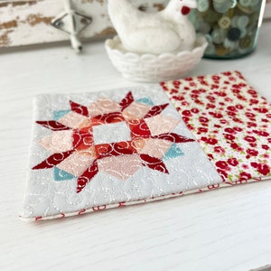 Peut inclure: Un dessous de verre matelassé rouge, blanc et bleu avec un motif en étoile. Le dessous de verre est en tissu et a un imprimé floral au dos.