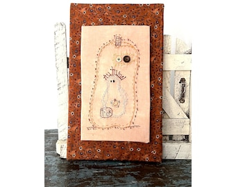 May include: A brown fabric wall hanging with a stitched design of a ghost in a pumpkin with the text "Autumn Trick".