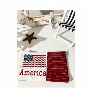 May include: A white and red quilted coaster with an embroidered American flag and the word "America".