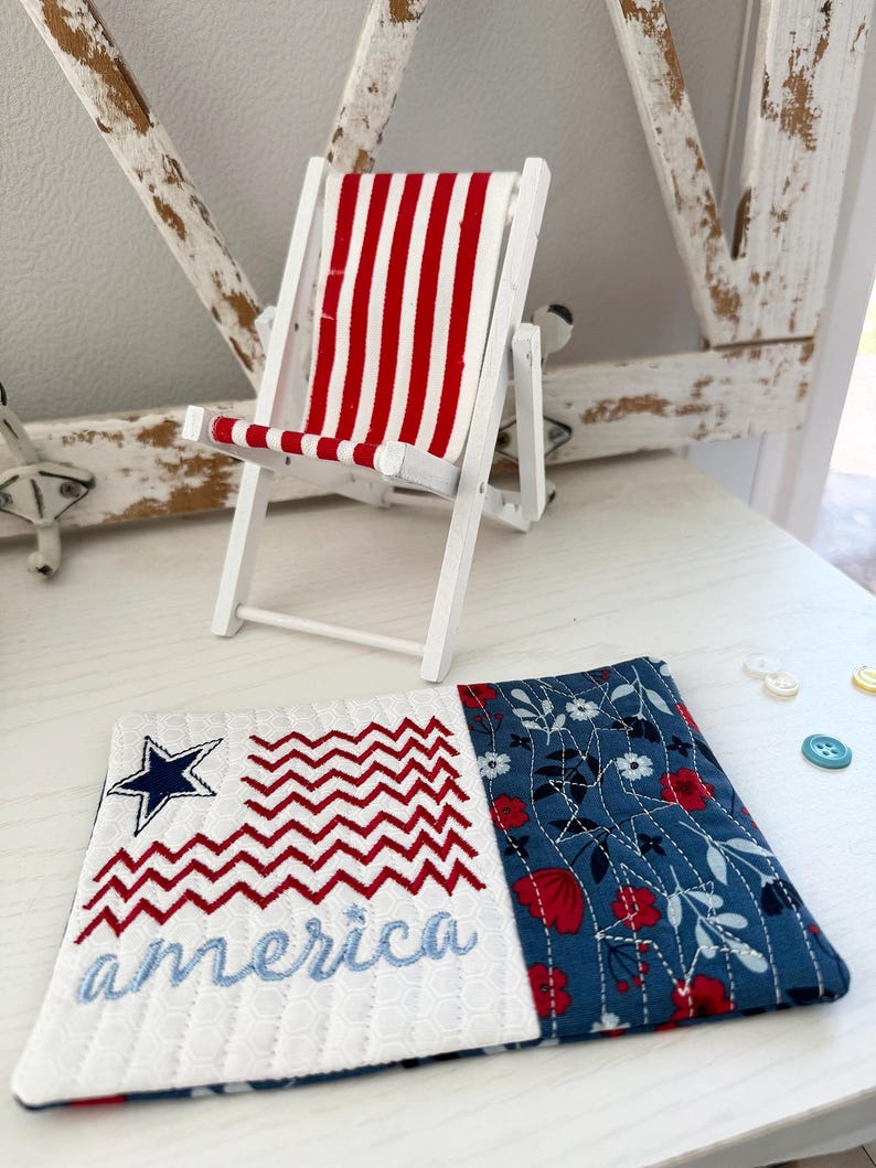Pu&ograve; includere: Una sedia a sdraio in legno bianco in miniatura con tessuto a righe rosse e bianche. Un sottobicchiere trapuntato con un disegno della bandiera americana ricamato e la parola "America" in blu. Il sottobicchiere ha un motivo floreale sul lato destro.