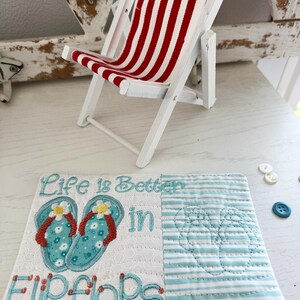 Pu&ograve; includere: Una sedia a sdraio in legno bianco in miniatura con tessuto a righe rosse e bianche. Un sottobicchiere decorativo trapuntato con la scritta "Life is Better in Flip Flops" e disegni di infradito ricamati.