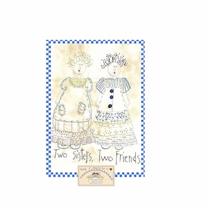 Op de afbeelding: Borduurwerk met twee zussen, gekleed in kleurrijke jurken, met de tekst "Two Sisters, Two Friends." Het kunstwerk is omlijst met een blauw-wit geblokte rand en bevat een klein logo onderaan.