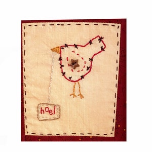 May include: A red embroidered bird with a star button on its chest is holding a small sign that says "hoel" on a cream-colored background. The background is surrounded by a red stitched border.
