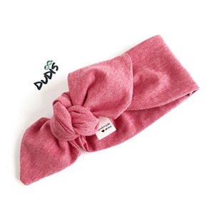 Puede incluir: Una diadema rosa anudada con una peque&ntilde;a etiqueta blanca que dice "hecho a mano con amor".