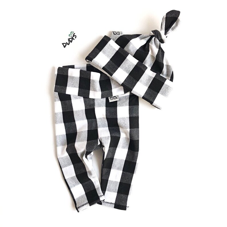 May include: Black and white checkered leggings and matching hat for a baby. The hat has a knot on top. The leggings have a fold-over waistband.