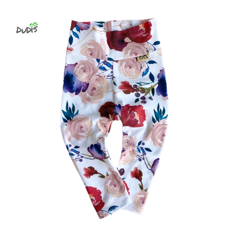 May include: White leggings with a floral print featuring pink, red, and blue watercolor flowers. The leggings have a high waist and a small brown label with the text "OOA" on the right side.