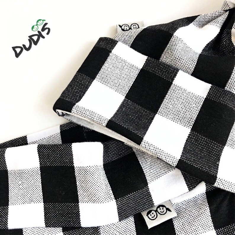 May include: Black and white checkered fabric with a white label that says "DUDIS" and a smaller white label with two smiling faces.