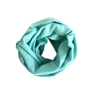 May include: A light turquoise infinity scarf made of soft fabric. The scarf is rolled up into a circle shape.