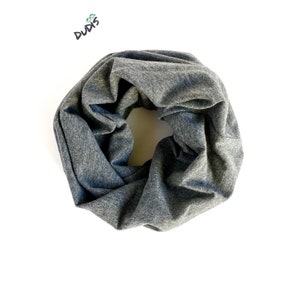 May include: A gray infinity scarf made of soft fabric. The scarf is a continuous loop, designed to be worn around the neck. The fabric has a heathered appearance, with variations in the gray color. The scarf is displayed on a white background.