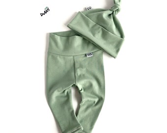May include: A sage green baby outfit set with a knotted beanie and leggings. The beanie and leggings have a small white tag with the word "DUDS" on it.