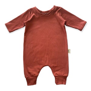 May include: A rust-colored ribbed long-sleeved baby onesie with a round neckline.