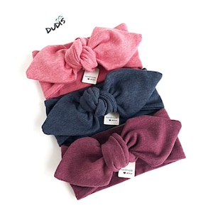 Puede incluir: Tres diademas anudadas en rosa, azul marino y burdeos. Cada diadema tiene una peque&ntilde;a etiqueta que dice "hecho a mano con amor".
