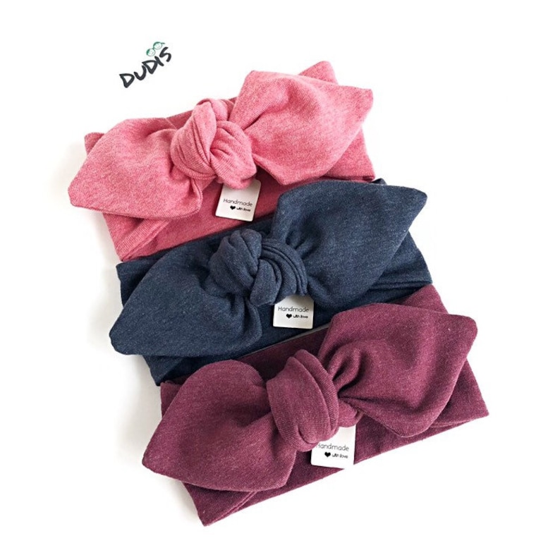 Puede incluir: Tres diademas anudadas en rosa, azul marino y burdeos. Cada diadema tiene una peque&ntilde;a etiqueta que dice "hecho a mano con amor".