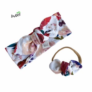May include: A set of two floral print headbands. The larger headband is tied in a bow and has a white background with red, pink, and purple flowers. The smaller headband is a nude elastic with a matching floral print bow. The tag on the larger headband reads "Handmade with Love".