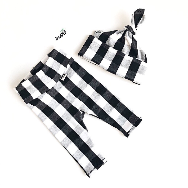 May include: Black and white checkered baby leggings and a matching knotted beanie. The leggings have a fold-over waistband and the beanie has a small tag with the word "Duds" on it.