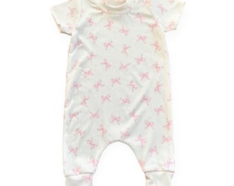 May include: A white baby romper with a ribbed texture and short sleeves. The romper is patterned with pink bows. The cuffs and neckline are ribbed. The garment is designed for comfort and ease of movement.