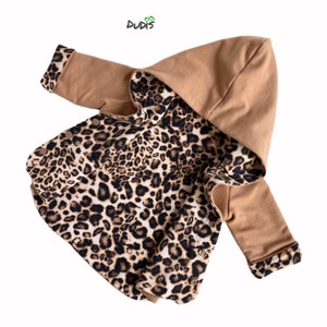 May include: A tan hooded jacket with a leopard print lining and accents. The jacket has long sleeves and a button-up front. The cuffs and hood lining feature the leopard print. The brand name "DUDIS" is visible in the top left corner.