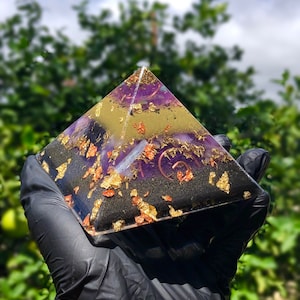 Può includere: Una piramide trasparente con un designo nero, viola e oro. La piramide è decorata con scaglie dorate e macchie di rame.
