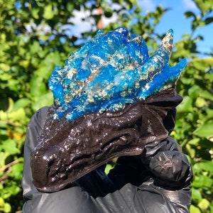 May include: A blue and black resin dragon head sculpture with gold glitter accents. The sculpture is being held by a gloved hand.