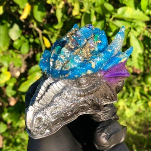 May include: A blue and silver dragon head sculpture with embedded crystals and gold flakes. The dragon head is made of resin and has a detailed, textured surface.
