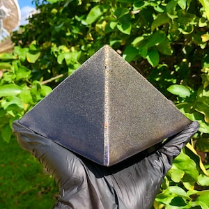 May include: A black pyramid-shaped object with a gold metallic finish. The object has a textured surface and a subtle sheen.
