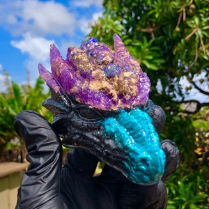 May include: A small, black dragon figurine with a purple and blue crystal head. The dragon's head is detailed with gold glitter and has a textured, scaly appearance.
