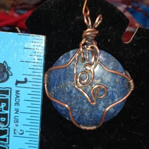 May include: A copper wire wrapped pendant featuring a blue lapis lazuli stone with gold flecks. The pendant is approximately 1 inch in diameter.